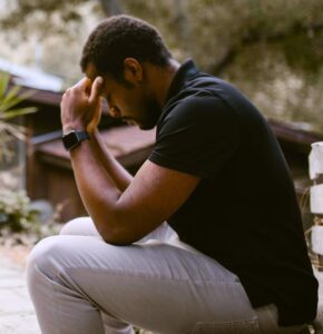 man sitting outdoors with head in hands
