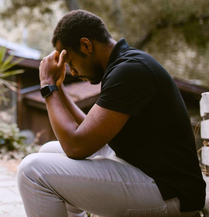 man sitting outdoors with head in hands