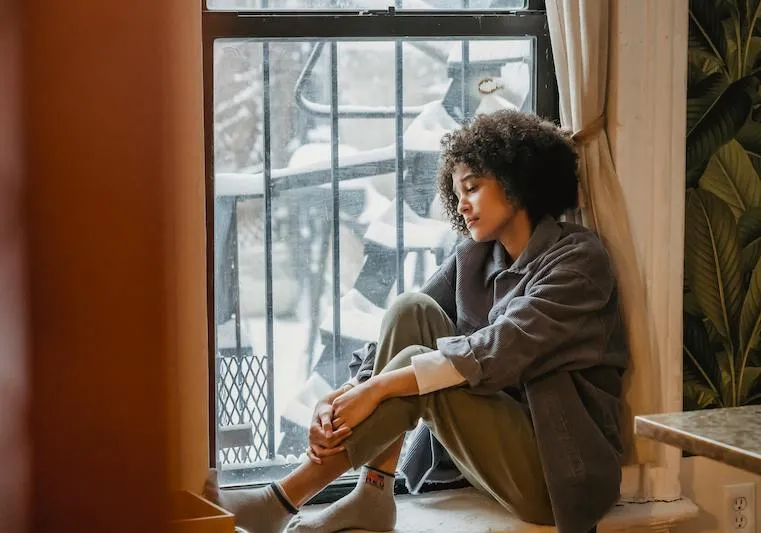 woman sitting on window sill looking sad