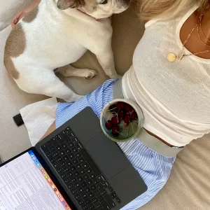 woman sitting with dog, laptop and bowl of cherries on her lap