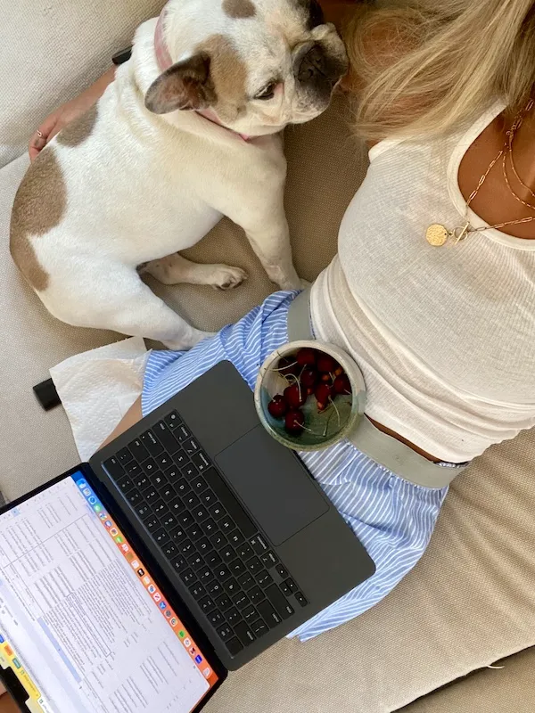woman sitting with dog, laptop and bowl of cherries on her lap