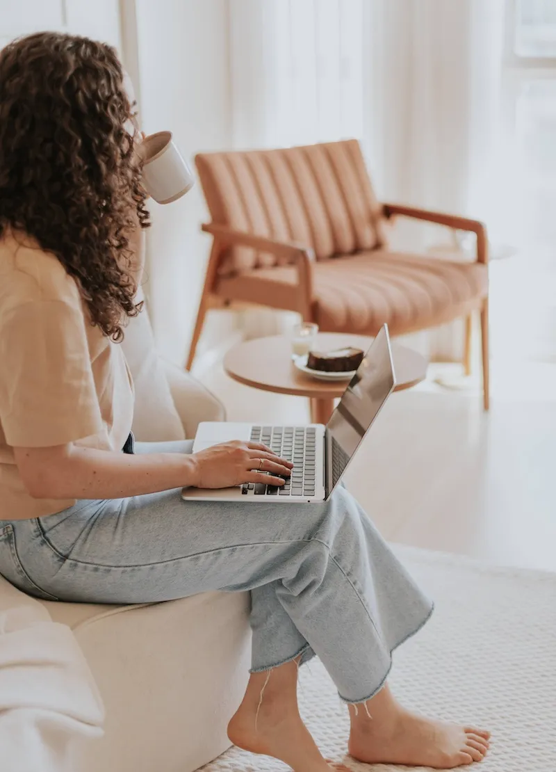 woman with laptop on knee drinking coffee